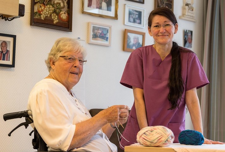Eine Pflegefachkraft steht neben einer Seniorin, die sich mit Wollarbeiten beschäftigt. Symbolbild. © Deutscher Caritasverband e.V./Pedro Citoler